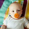 A toddler sucking on an orange Shushie pacifier